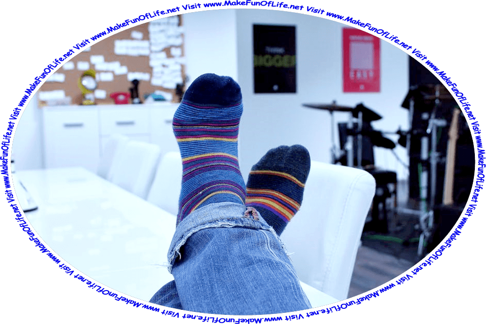 Picture of a person’s shoeless feet propped up on a table, while wearing dark blue socks with thin red, yellow, and light blue stripes, and the words, ‘Visit www.MakeFunOfLife.net.’